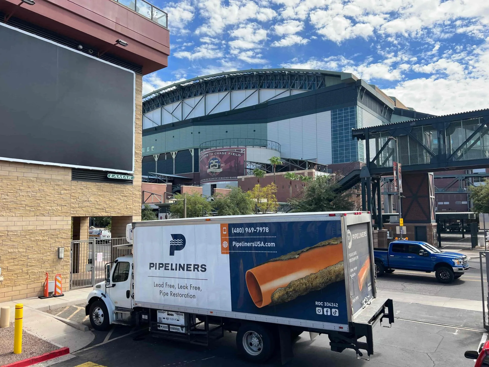 Pipeliners USA delivery truck outside a stadium, showcasing company branding and contact info in a bustling urban setting.