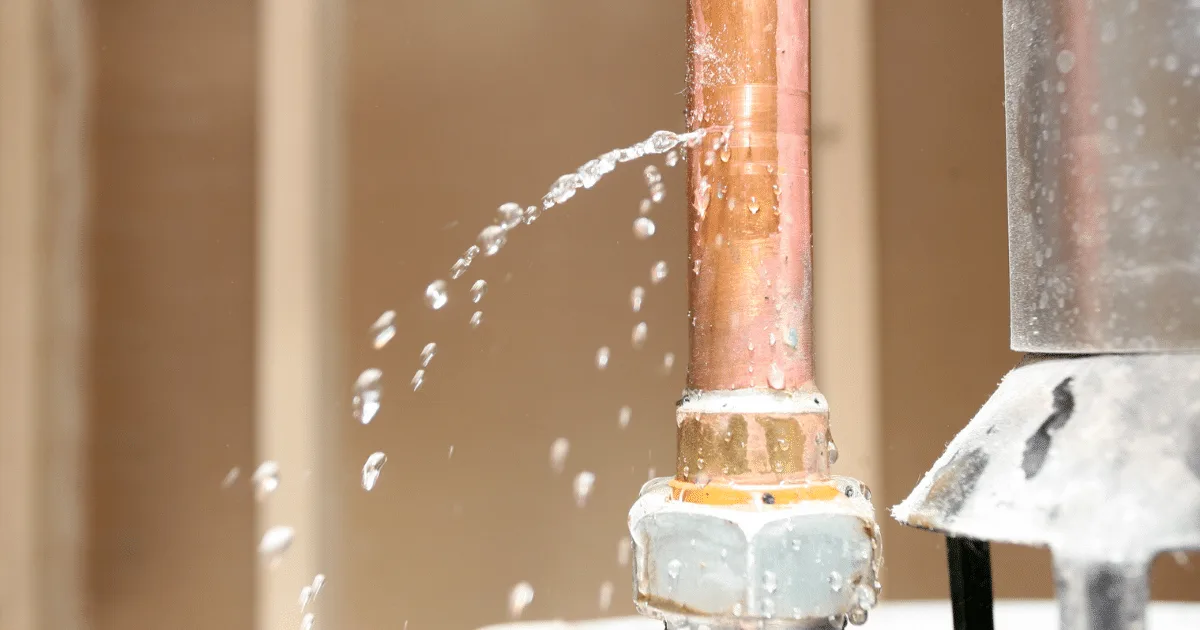 Copper pipe with a pinhole leak spraying water, illustrating plumbing issues related to home repairs and maintenance.