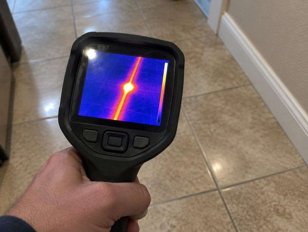 Thermal camera screen showing a warm hot water line under a tile floor with a bright spot where the slab leak is